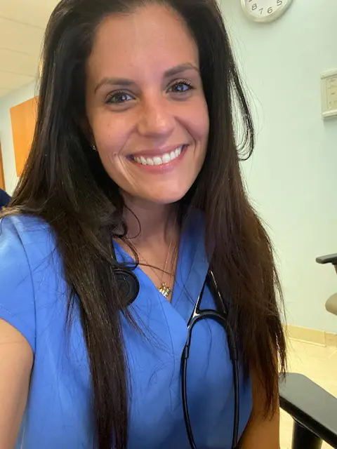 A woman in blue scrubs smiling for the camera.